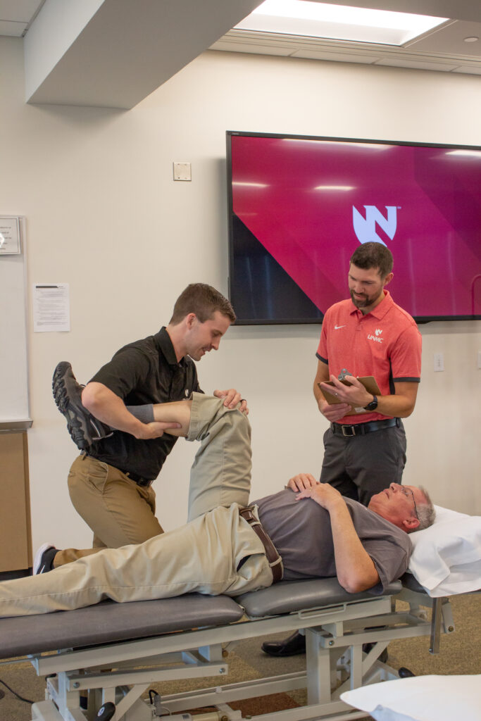Faculty looking on as an Orthopedic PT resident checks a patient's range of motion.