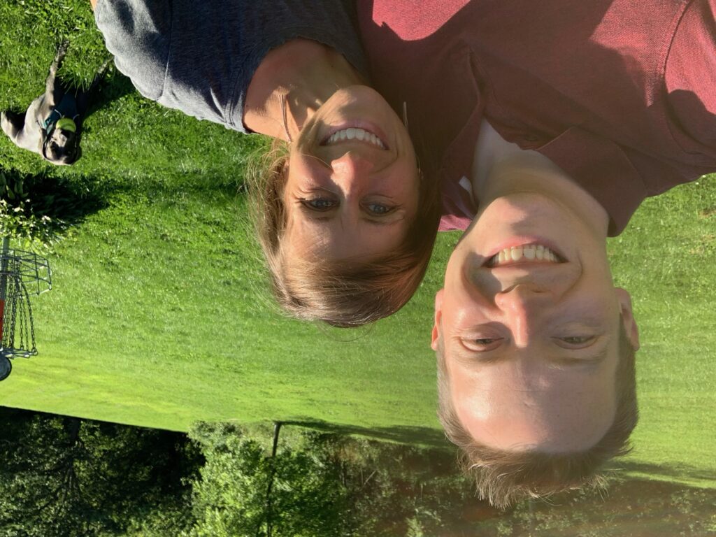 photo of Dr. McElroy and his wife in a green field with their dog in the background behind them