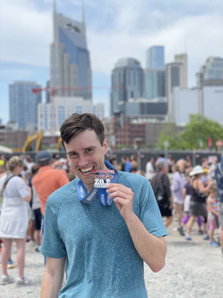 person holding up a medal in foreground. in background many people and tall buildings