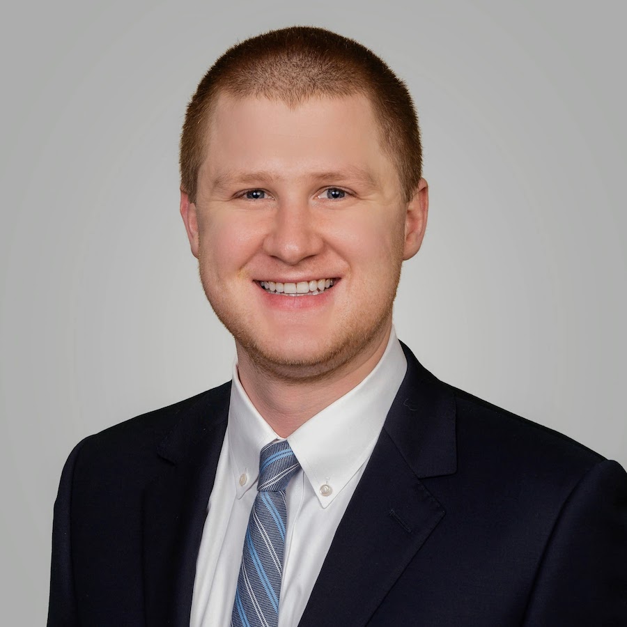 headshot of smiling man wearing a black jacket and blue striped tie