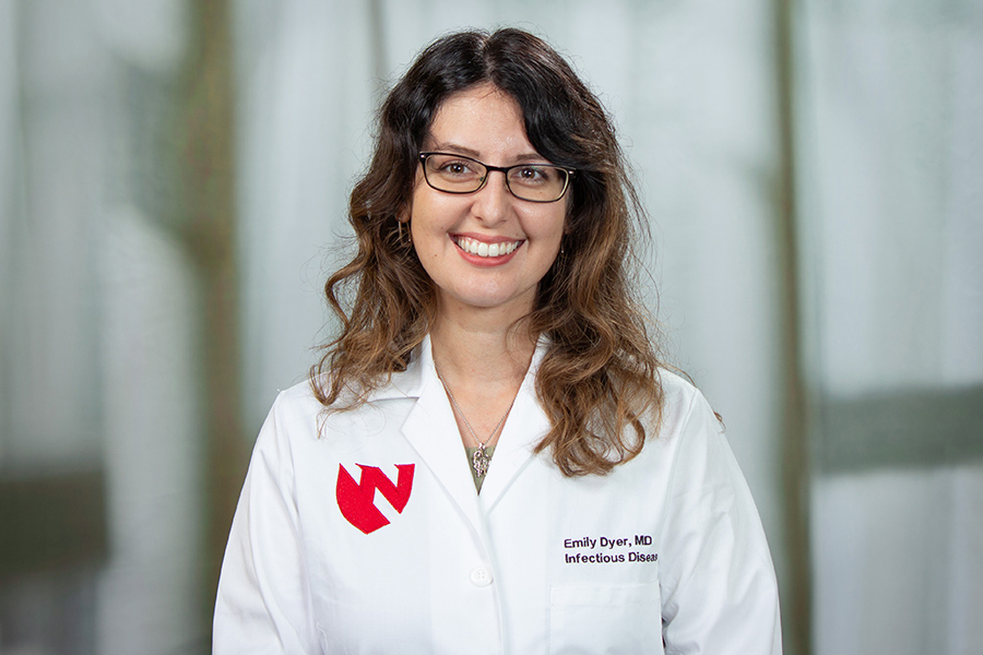woman with long brown hair wearing glasses, smiling, wearing a white coat