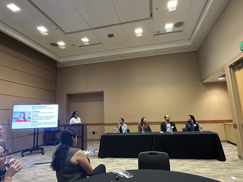Moderator introduces a panel of four speakers during a conference career development session, with attendees seated in the audience and a presentation slide displayed nearby.
