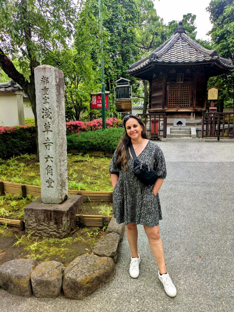 Person standing on a pathway beside a stone marker and traditional temple building.