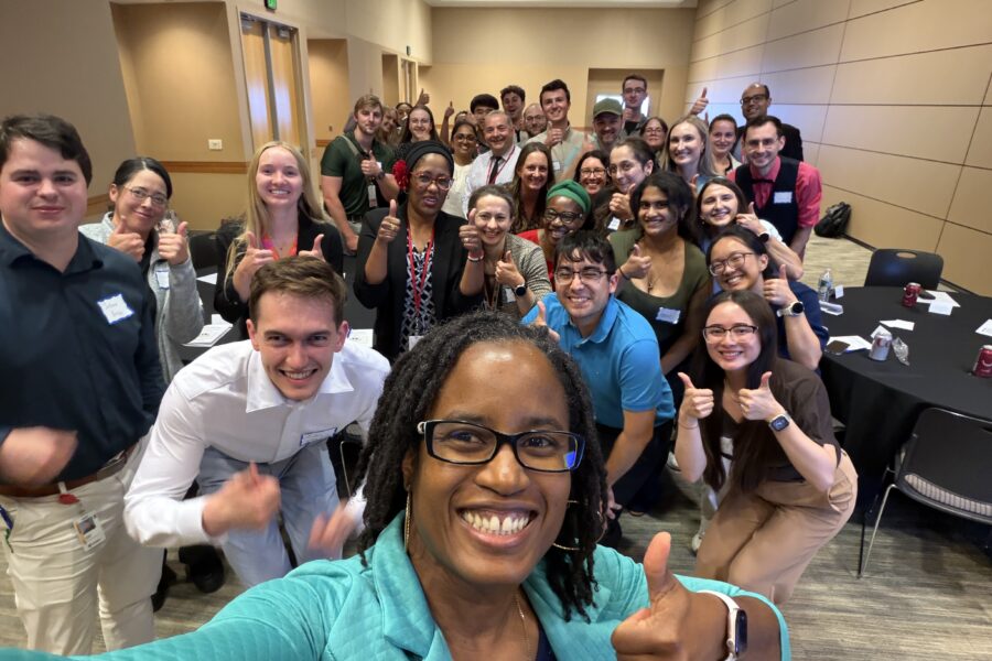 Large group of conference attendees gathered for a group photo after a professional development and networking session, with many participants giving thumbs-up gestures