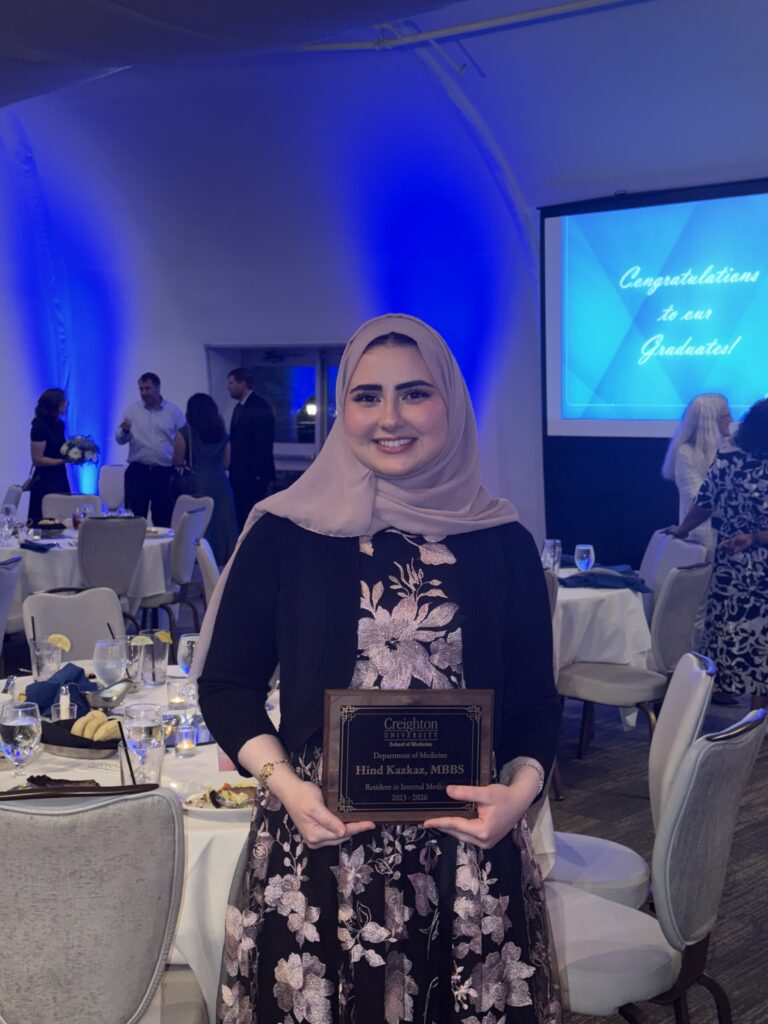 Person holding an award plaque at a graduation banquet, standing in front of tables and blue-lit event décor.