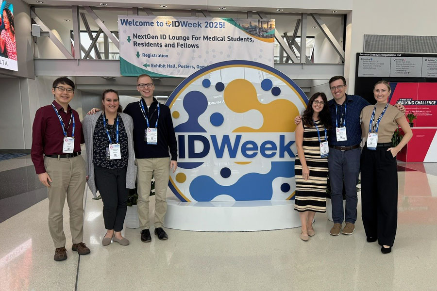 Conference attendees pose around a large circular IDWeek sign in the convention center lobby. 
