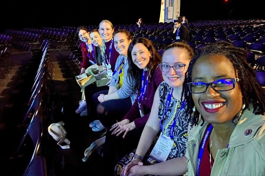 Seven IDWeek attendees sit together in the front row of a large conference auditorium before a session.