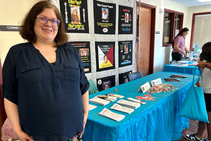 Kiara Comfort at the Santee Sioux Health Fair standing in front of a COVID remembrance quilt&period;