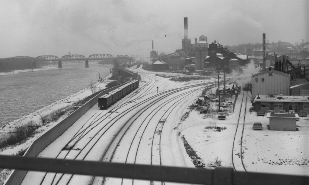 Black and white image of train from 1967 traveling along tracks in downtown Omaha by the Missouri River.