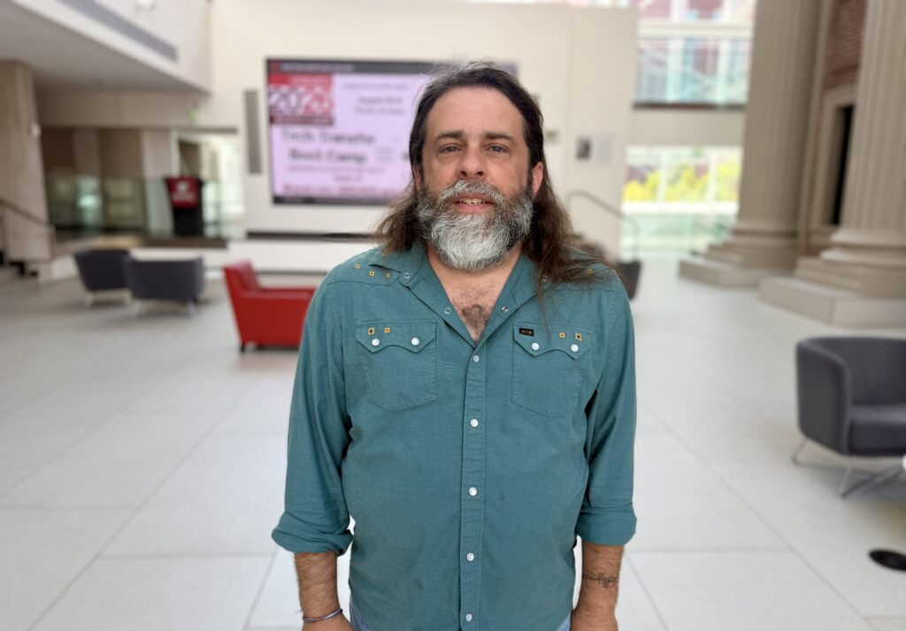 Man in teal green shirt in front of sitting area and screen