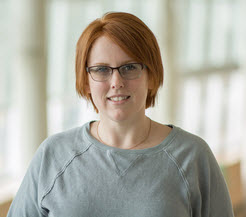 Danielle Westmark with reddish-orange hair in a gray top against lit windows