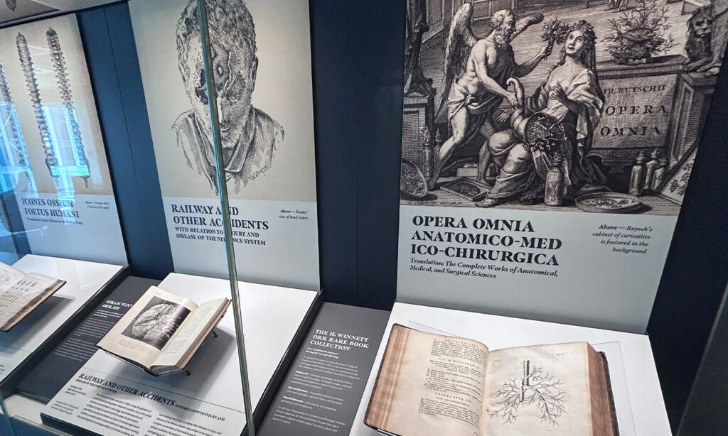 A number of rare books rest open underneath explanatory panels in the rare book gallery on Level 5 of Wigton Heritage Center.